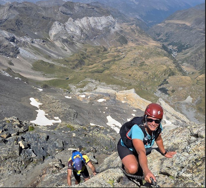 La Pau escalant una carena de muntanya, amb casc i material d'alta muntanya
