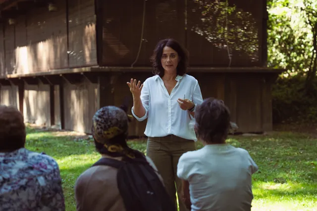 La Pau, dreta a l'aire lliure, parla i gesticula davant d'un grup de participants asseguts d'esquena durant un taller.